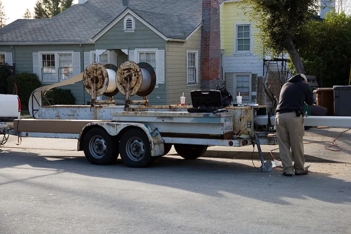 Worker at a trailer-mounted seamless aluminum gutter machine on a residential street