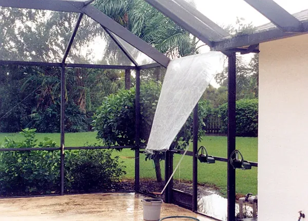 Torn screen panel hanging loose from a pool cage after a storm, Sarasota, FL