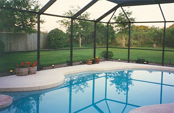 Freeform pool at dusk inside a dark-framed screen cage