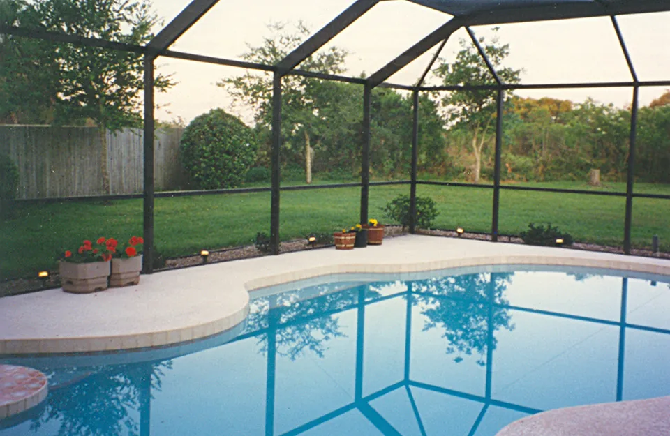Freeform pool at dusk inside a dark-framed screen cage