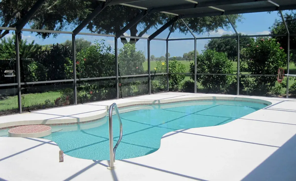 Freeform pool inside a dark-framed screen enclosure with an oak canopy beyond
