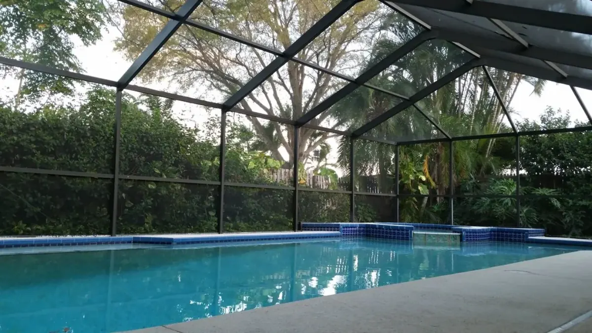 Rectangular pool inside a dark screen cage with tropical shrubs and oaks seen through the mesh