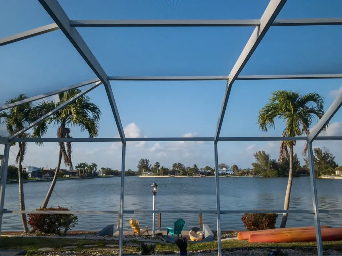 View through a white aluminum pool cage frame to a canal with palm trees, Cape Coral, FL