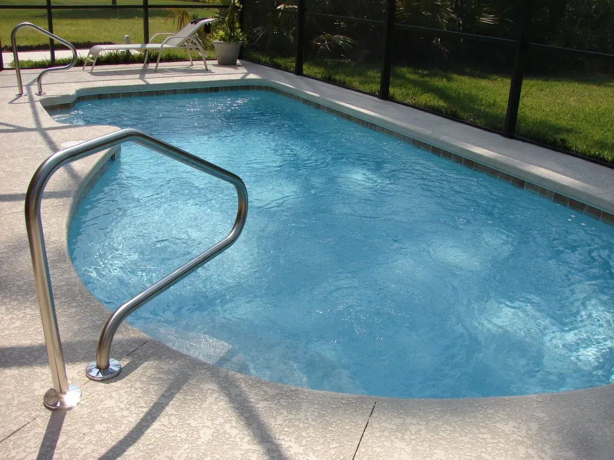 Pool with a steel handrail beside a dark screen enclosure wall and lounge chair