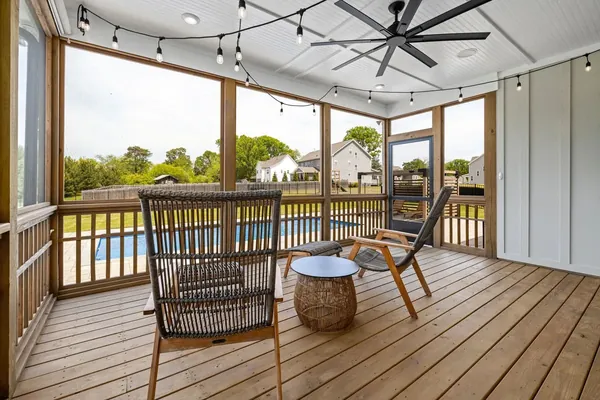 Screened porch with wicker chairs and a ceiling fan overlooking a pool