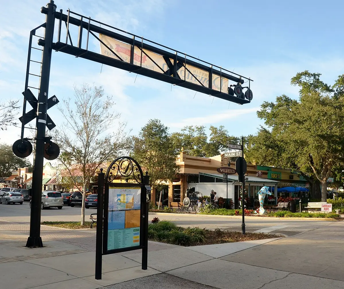 Downtown Dunedin street corner with shops, oak trees and a wayfinding map in Dunedin, FL