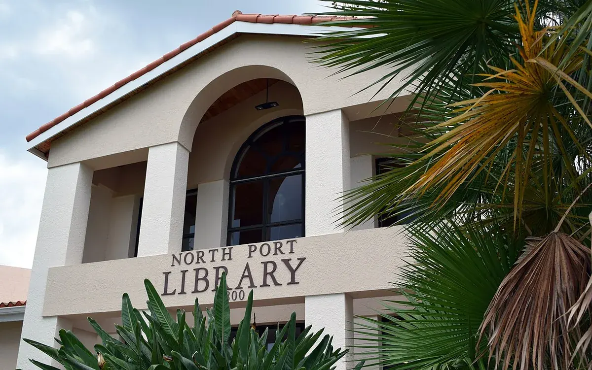 Arched cream facade of the North Port Library with palm fronds in North Port, FL